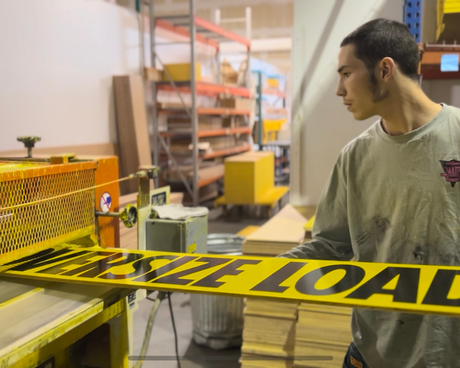Person standing next to an 'OVERSIZE LOAD' sign in a warehouse setting