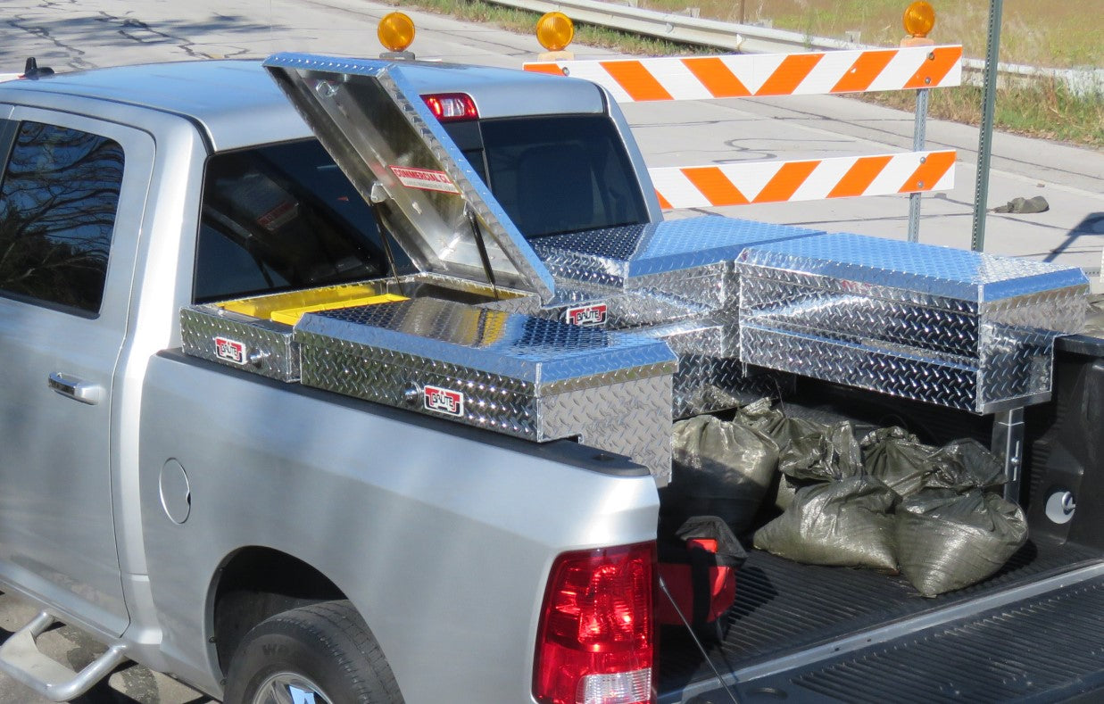 Silver truck with open gullwing toolbox in the back on a road commercial tool box